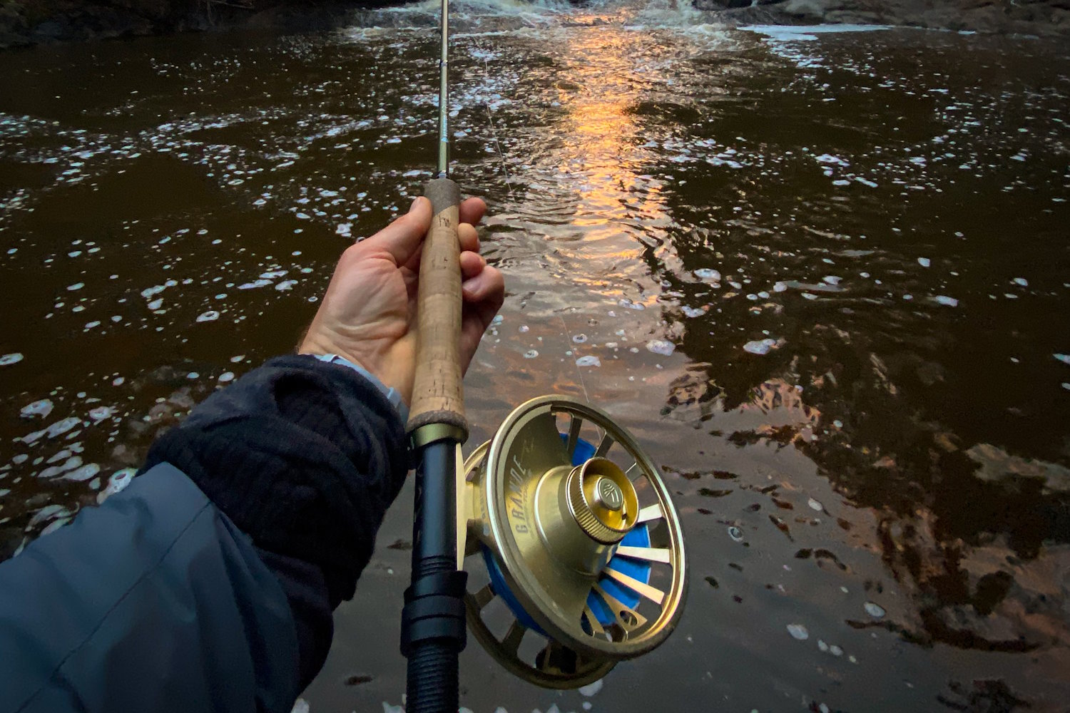 Holding a fly fishing rod over a river at sunset.