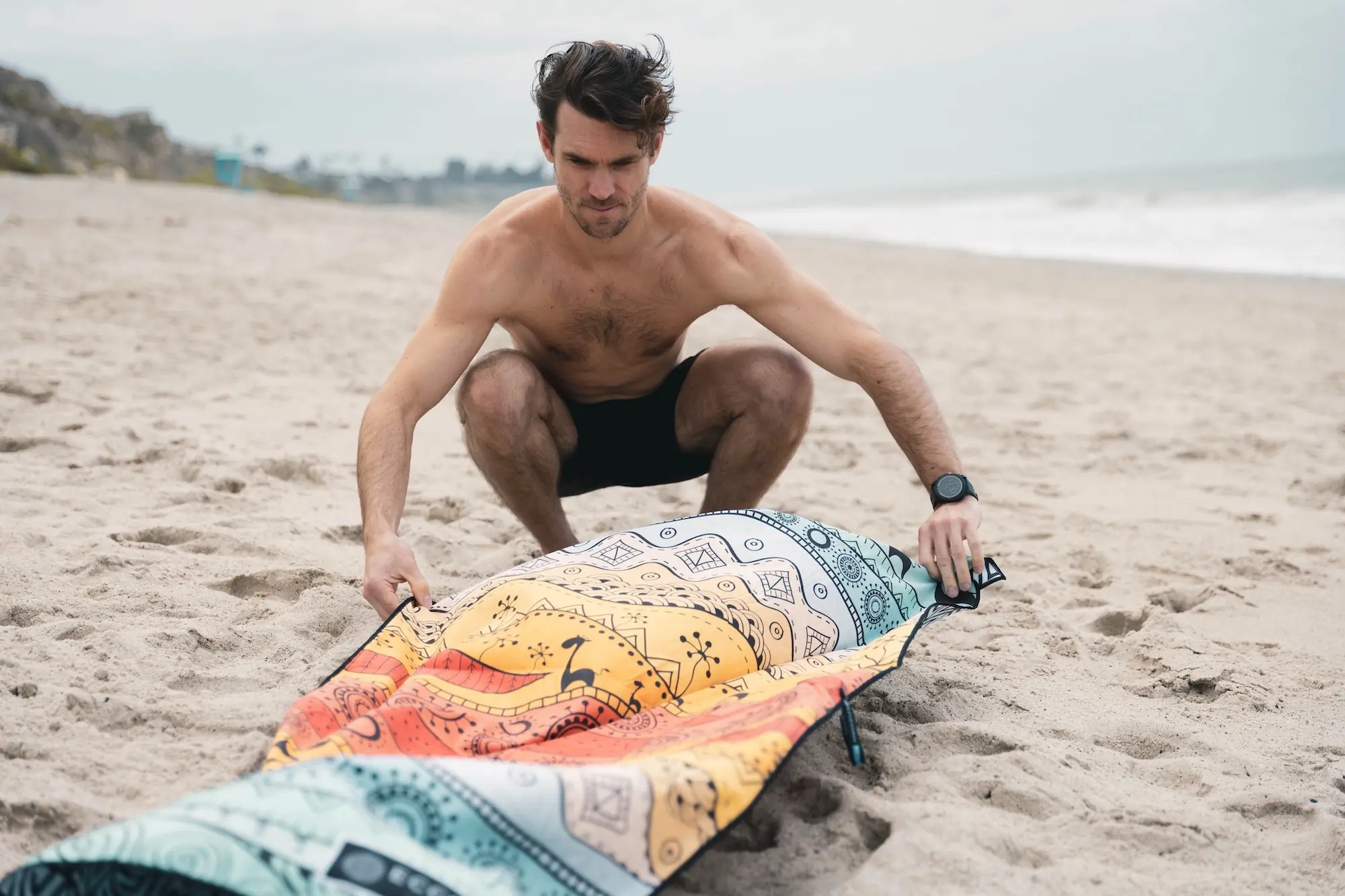 A man shaking the sand off of a microfiber beach towel at the beach