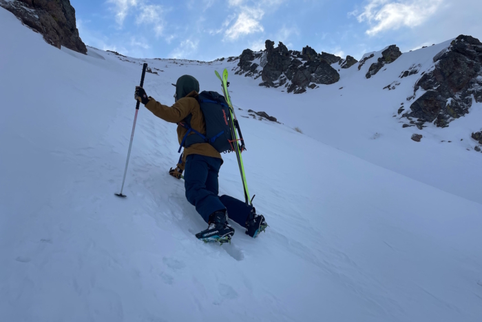 Skier climbing a steep snowy slope with poles.