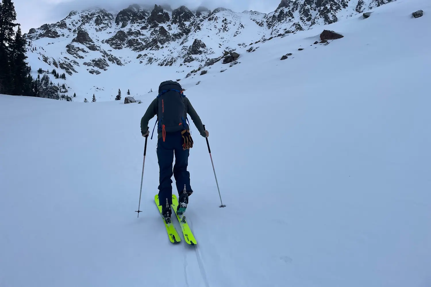 Skier ascending a snow-covered mountain slope with rocky peaks in the background