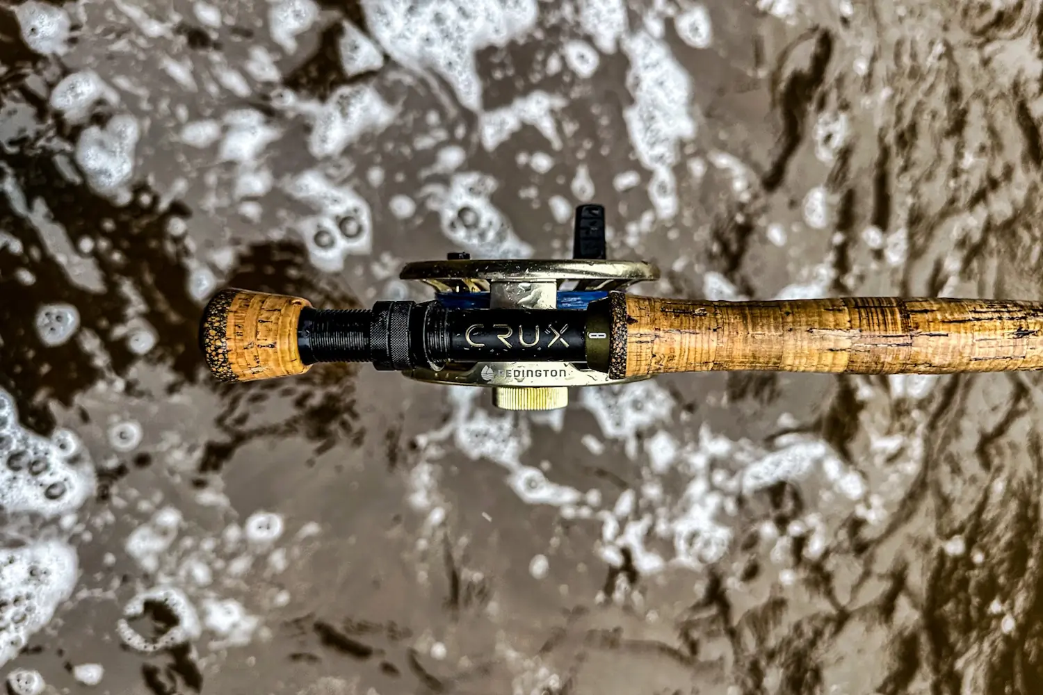 Close-up of a fly fishing rod handle and reel above swirling water