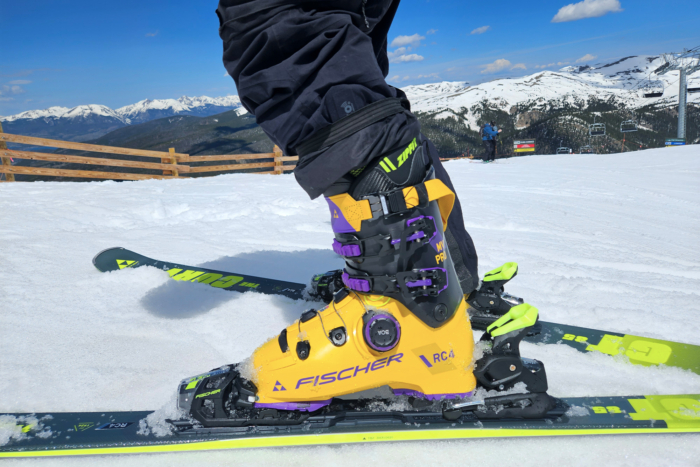 photo shows a man skiing, with the focus on his legs from the knees down. He is wearing bright yellow Fischer RC4 Pro MV BOA ski boots