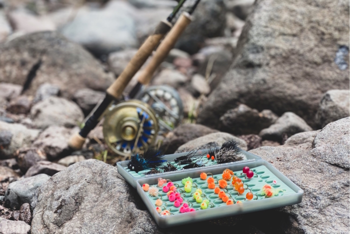 A fly fishing rod resting on rocks beside an open tackle box
