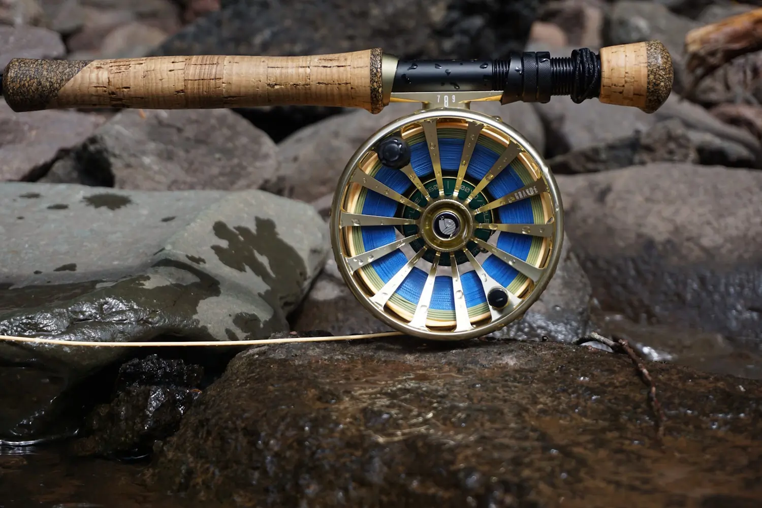 Close-up of a fly fishing rod and reel resting on wet rocks
