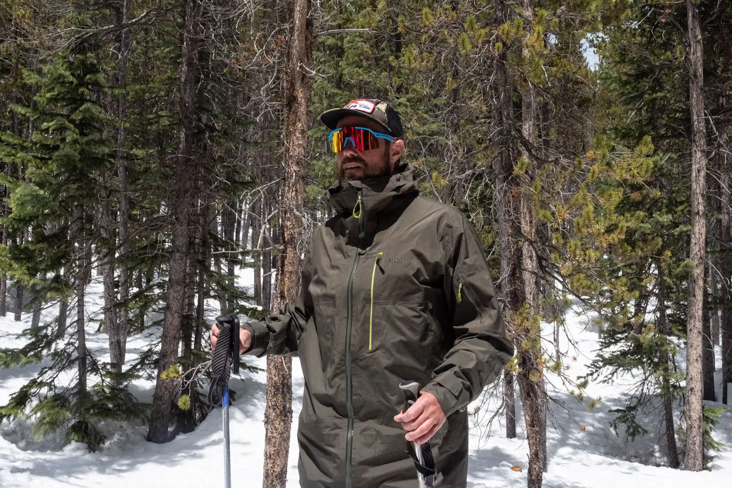 Man hiking in snowy forest wearing Rab Latok jacket and colorful sunglasses
