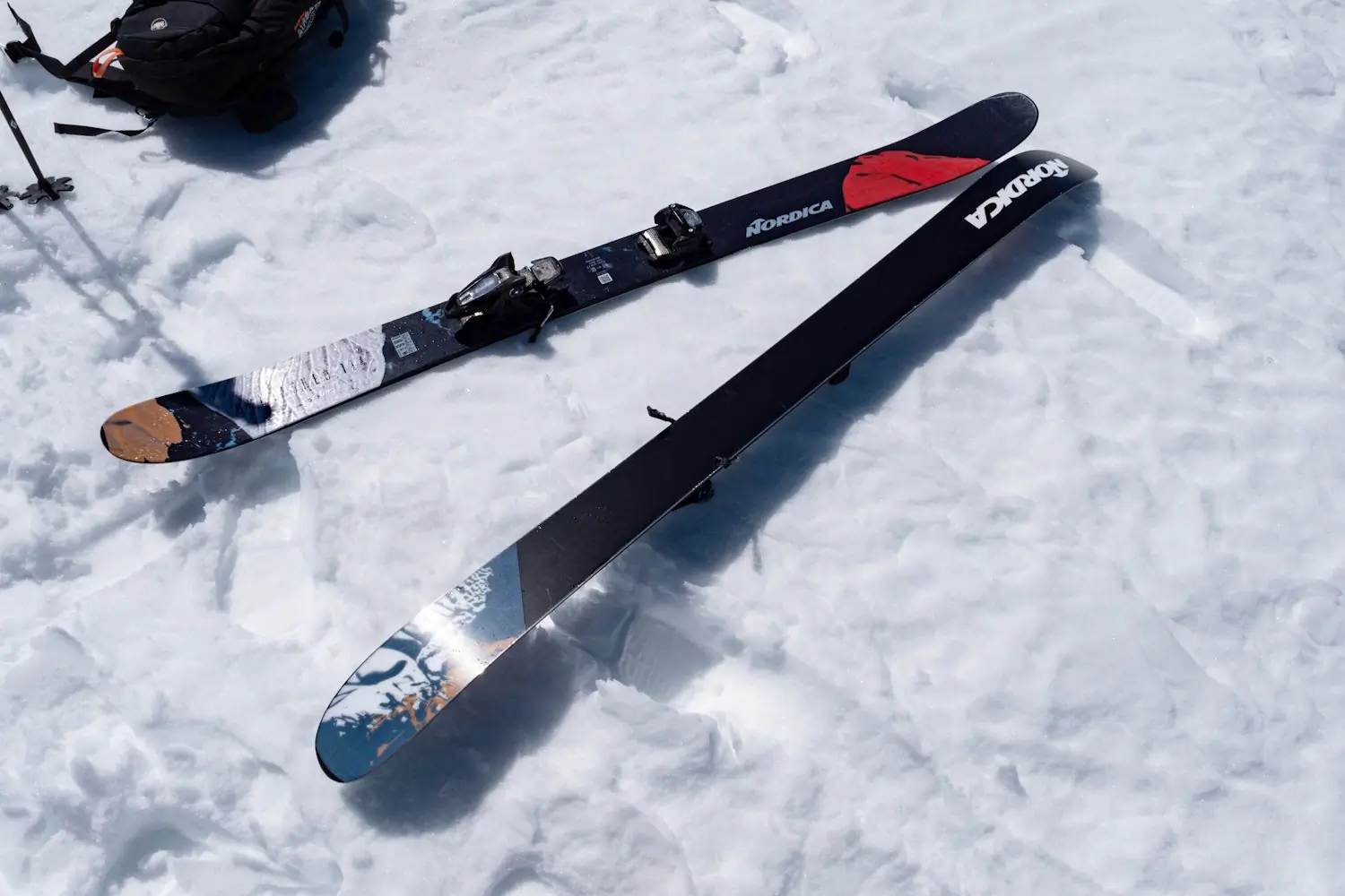 Nordica Unleashed 114 skis lying on snow next to ski poles and a backpack