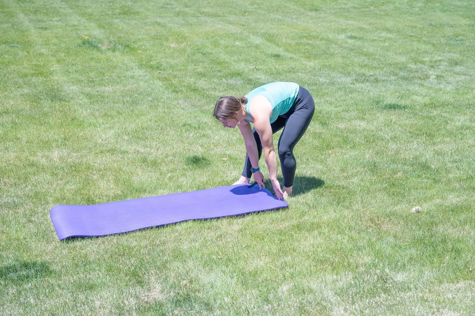 woman unrolling yoga mat on grass