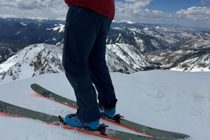 Skier standing on a snowy mountain peak with skis, overlooking a vast mountain range