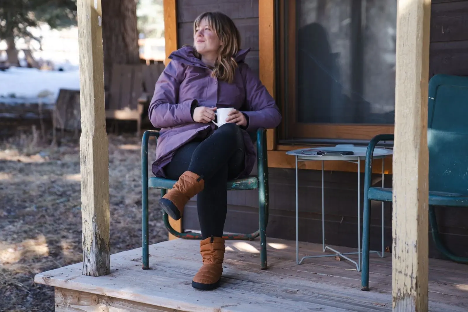 woman wearing sierra designs down booties while drinking coffee in front of the cabin