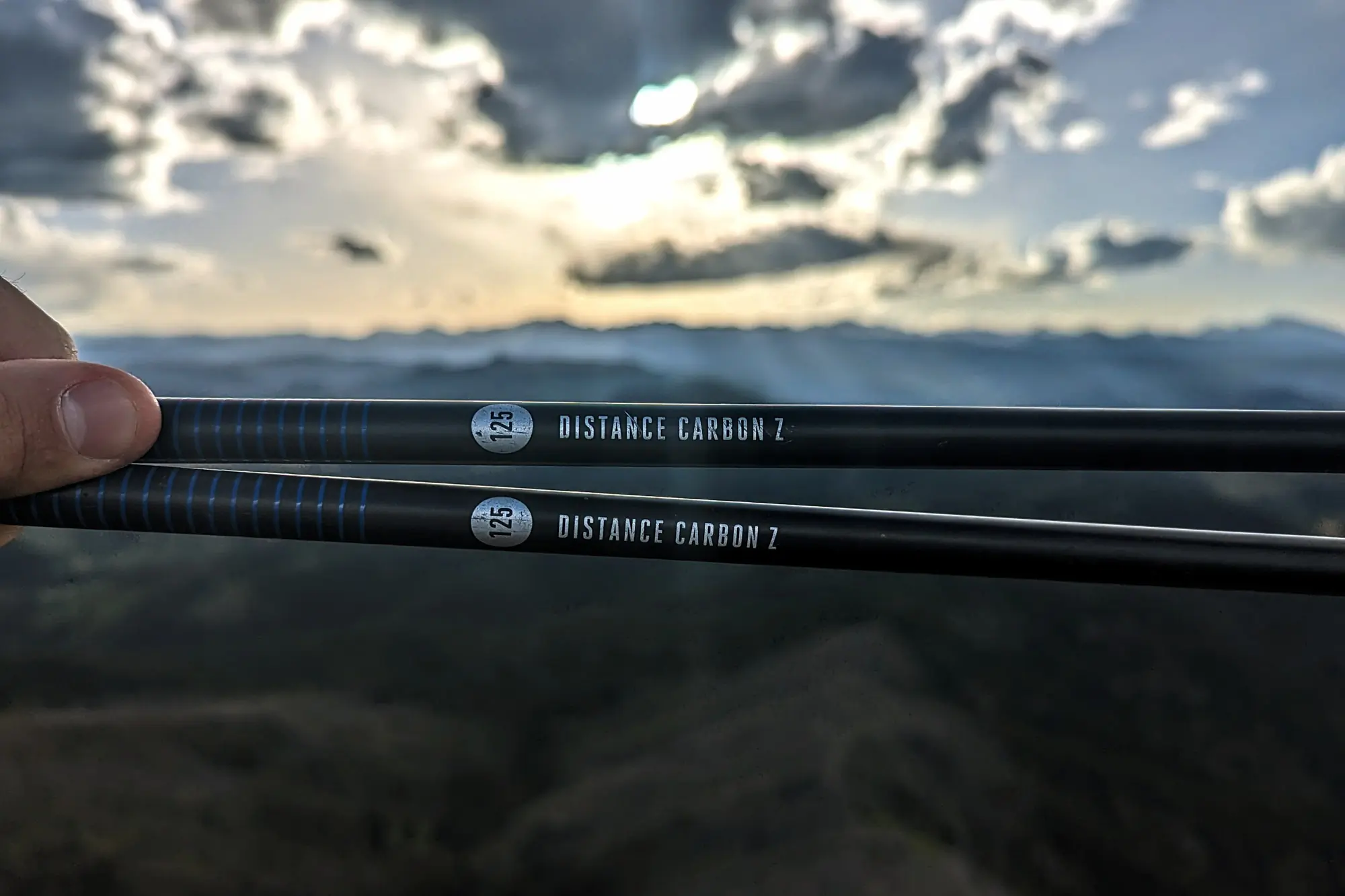 a runner holds the distance poles out in front of them, with a sunset in the background