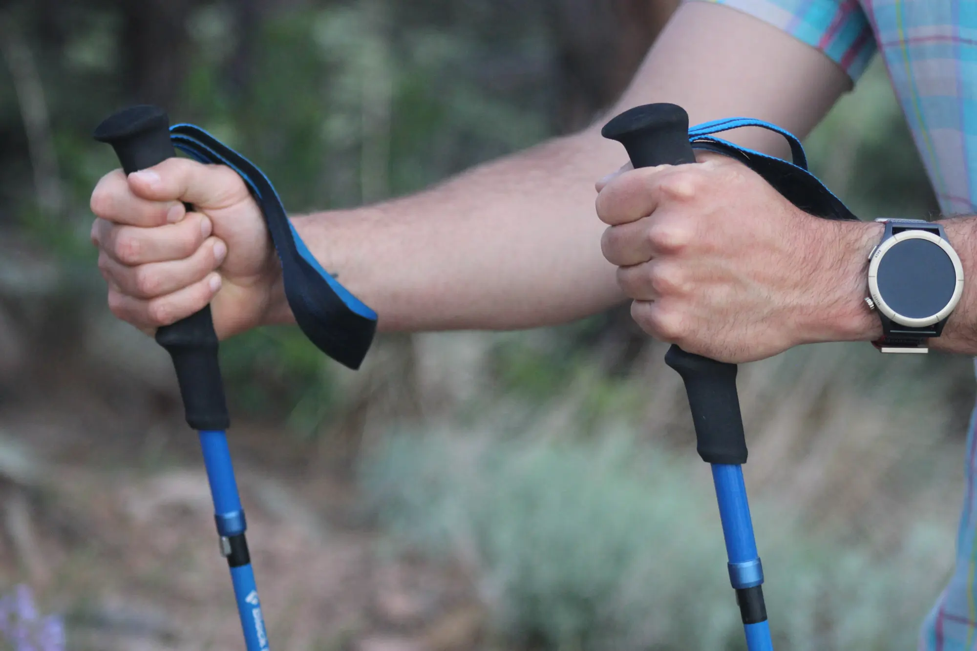 a hiker grips the two trekking poles, showing the EVA foam grips and wrist straps