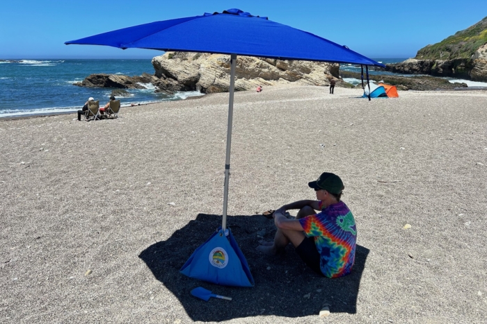 A man sitting at the beach in the shade of the BeachBUB All-In-One beach umbrella