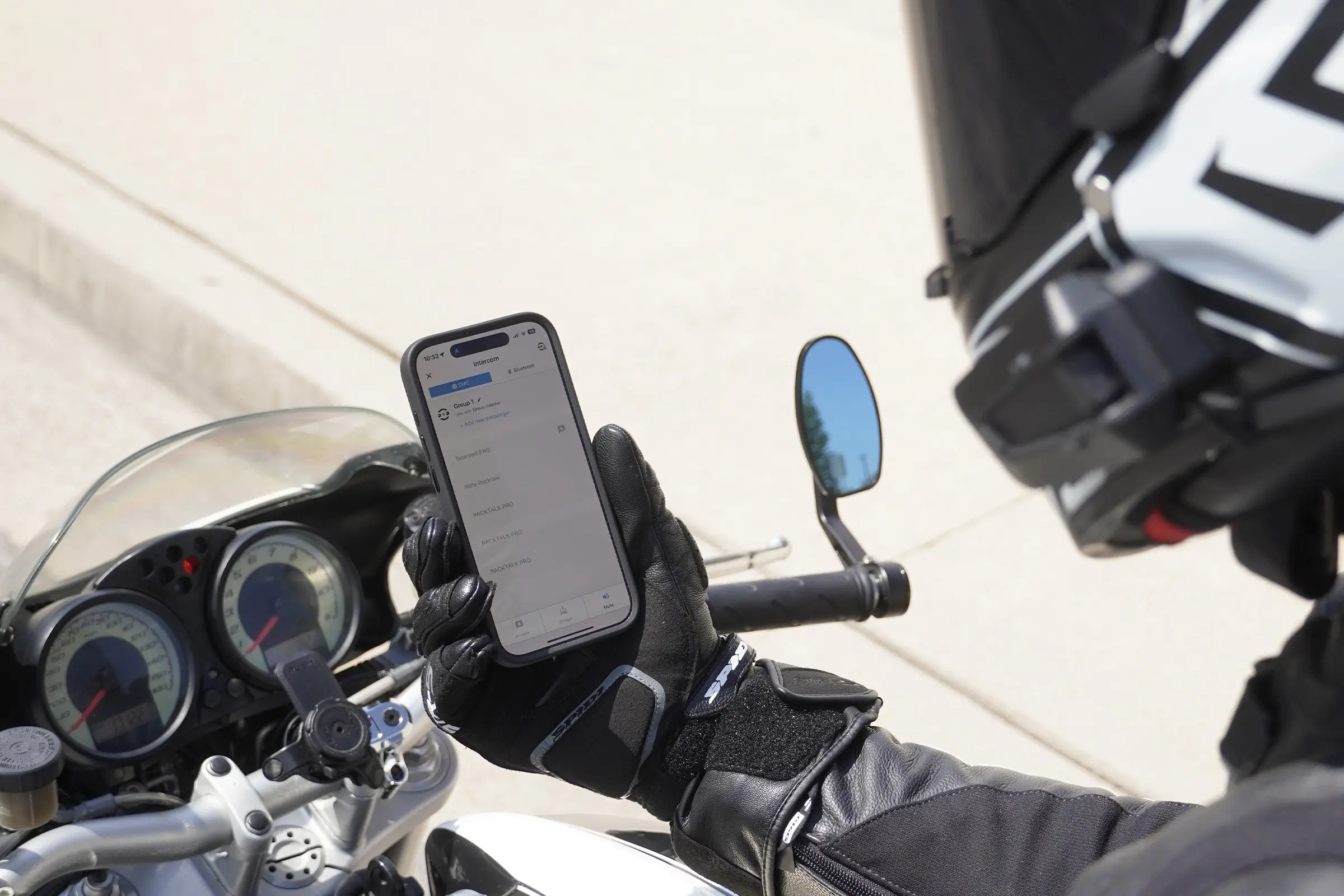 A motorcyclist holds a phone on the motorcycle, displaying the app with intercom feature on the screen