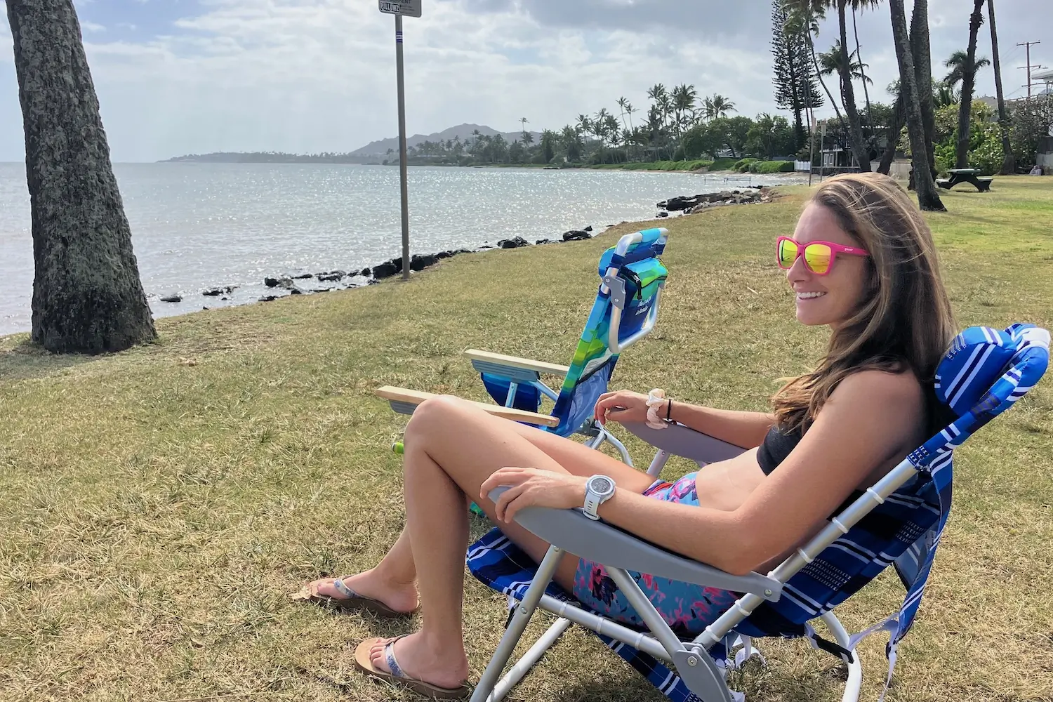 Rebecca Parsons sitting in a beach chair by the ocean in Hawaii while wearing the Goodr Pop G sunglasses