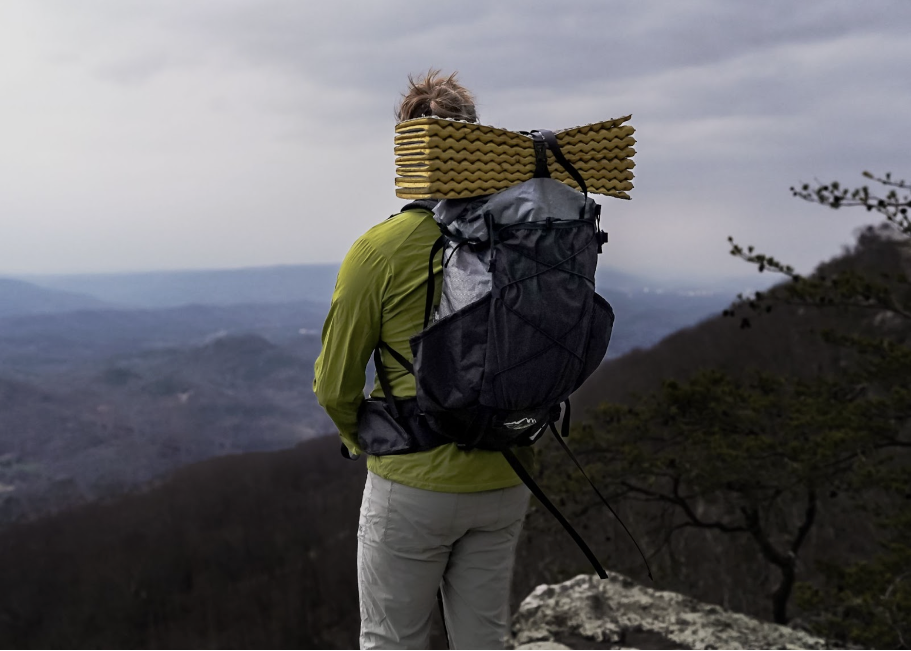 A hiker wears the ula ultra circuit pack with a foam pad strapped to the top