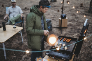 a strikingly handsome and fit 40-ish year old man cooking a camp dinner on the weber traveler griddle 22