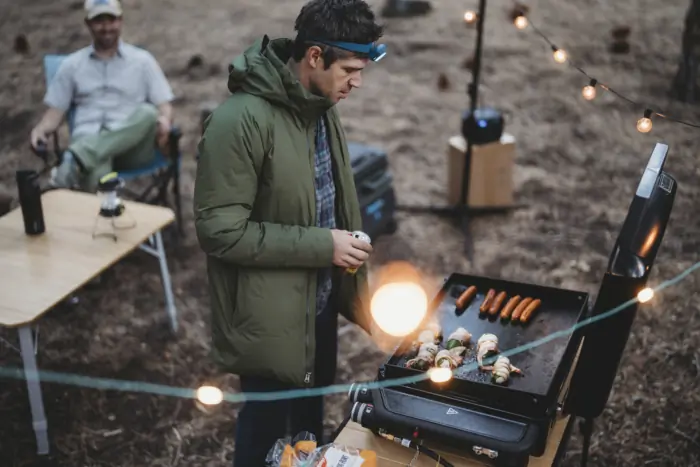 a strikingly handsome and fit 40-ish year old man cooking a camp dinner on the weber traveler griddle 22