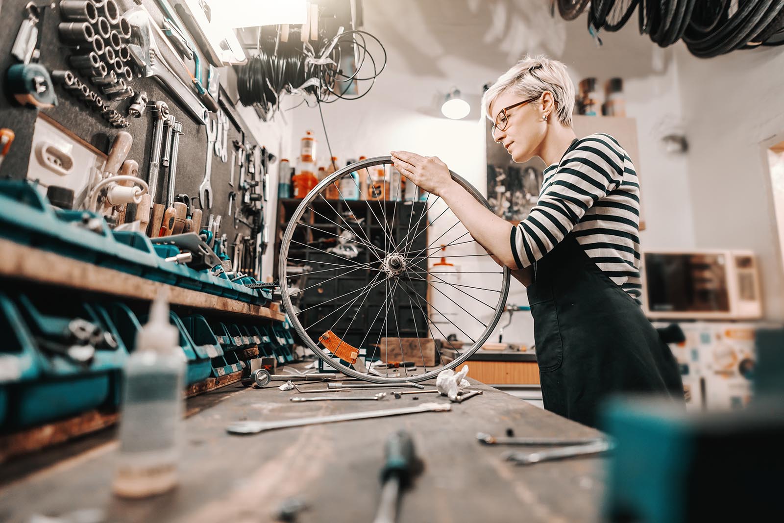 female worker holding and repairing bicycle wheel while standing in bicycle workshop.