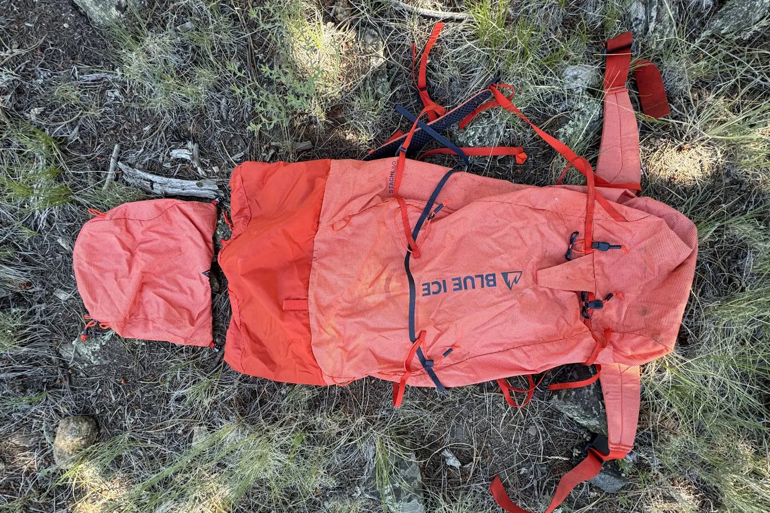Blue Ice Stache backpack in orange, laid on the ground with removable lid and the shoulder straps visible