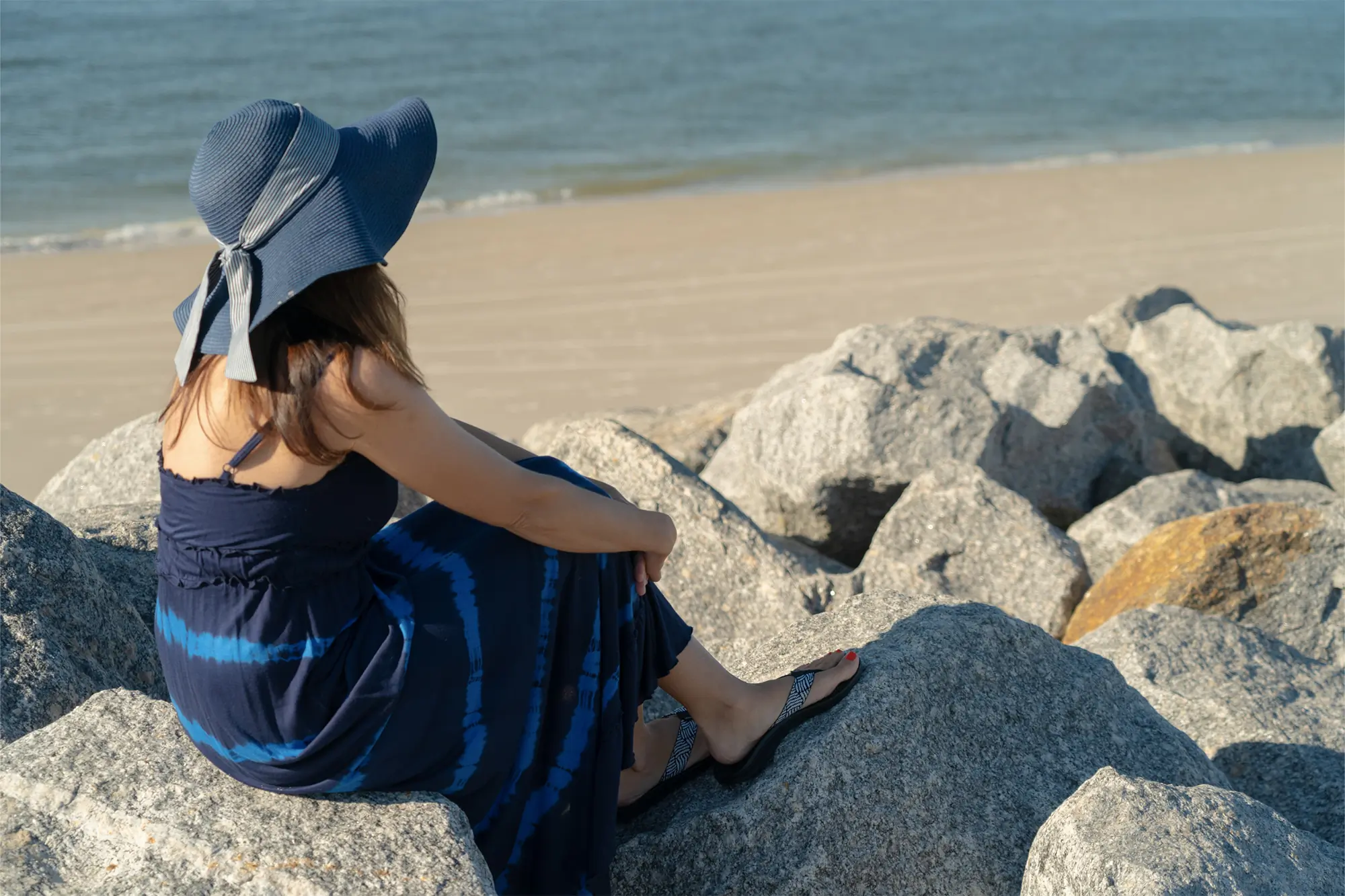 woman wearing dress and chaco flip flops sitting on the rocks at the beach
