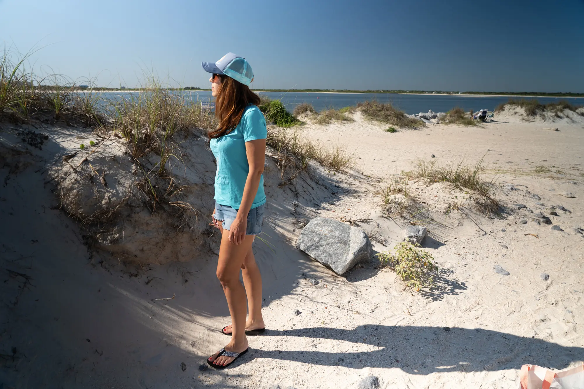 woman on the beach wearing chaco flips and bleu shirt