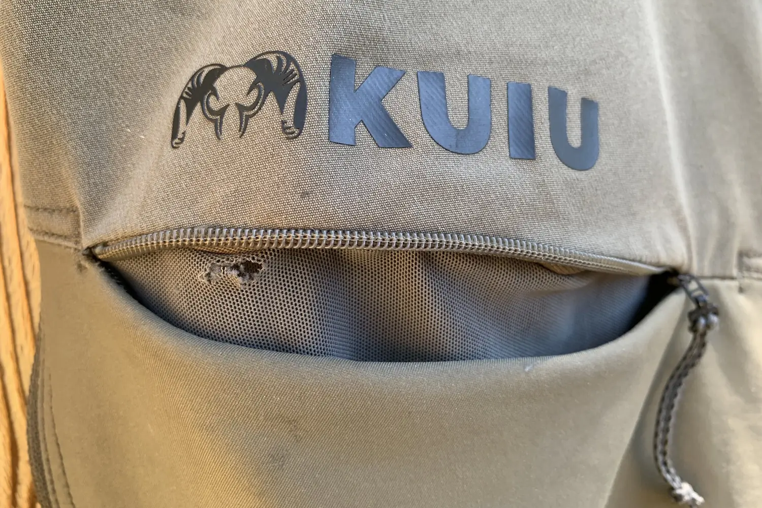 Close-up of a KUIU Women's PRO Brush pants showing a small hole and wear in the fabric near the logo