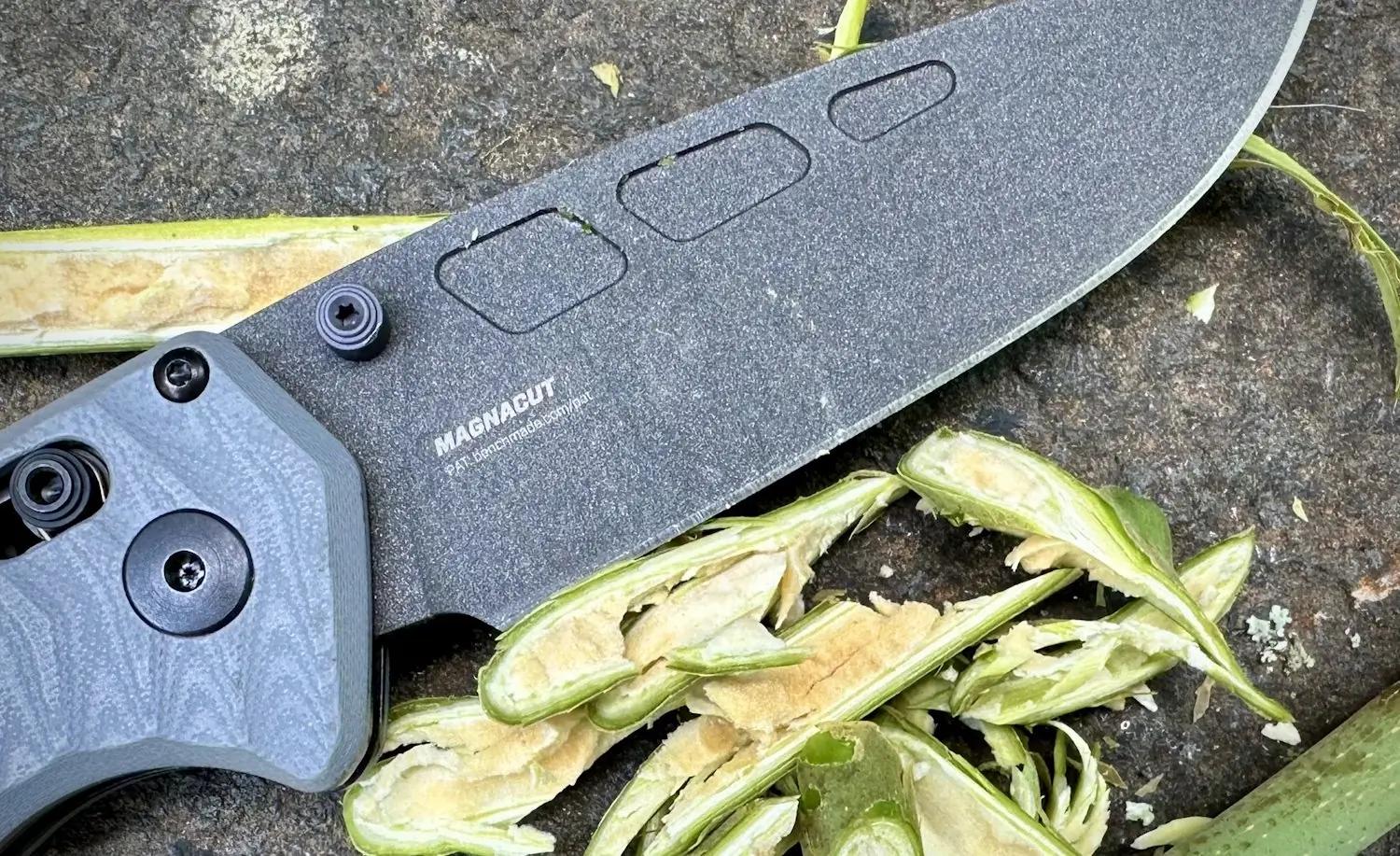 Close-up of a Benchmade knife with a Magnacut blade, showcasing its non-stick finish while cutting through green plant stems