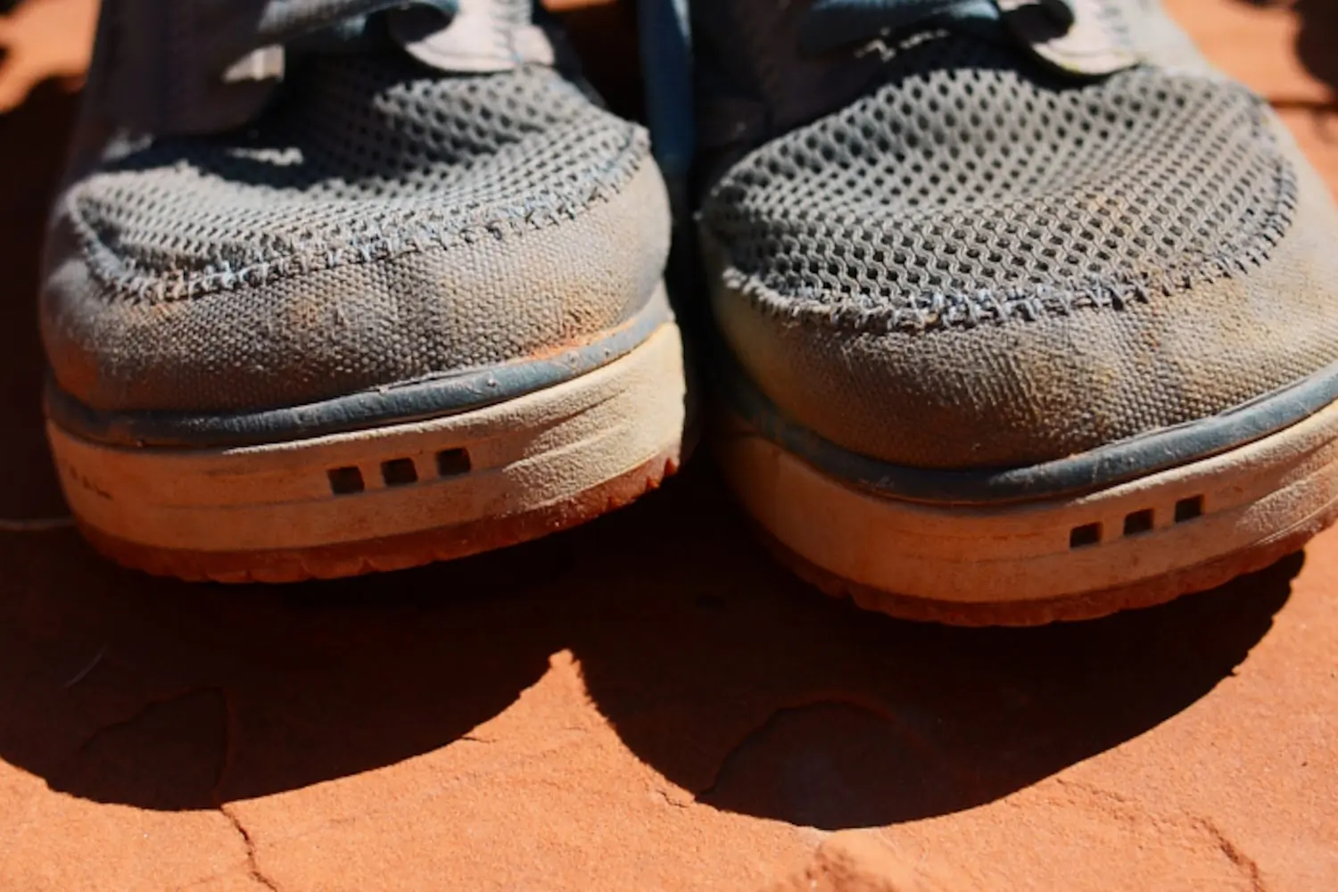 A pair of worn brewess 2.0 shoes on a red, textured surface, showing scuff marks and dirt