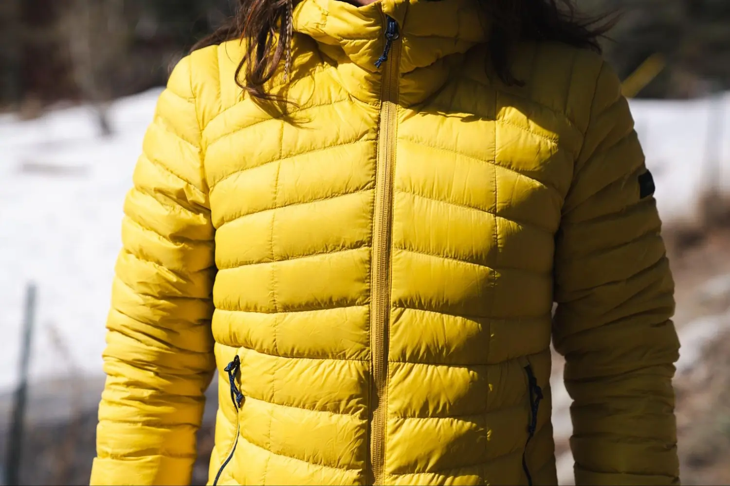 Close-up view of a person wearing a bright yellow puffer jacket with a front zipper and side pockets