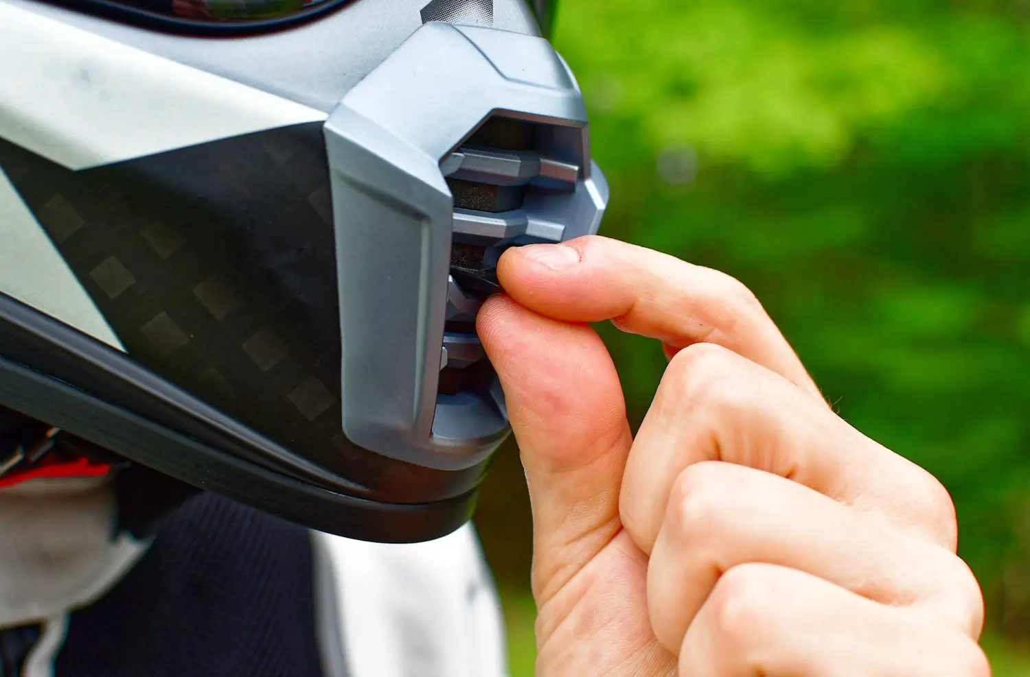 A close-up of a person's hand adjusting the vent on the mouthpiece of a Klim motorcycle helmet