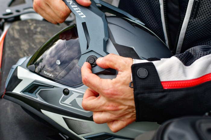 A close-up of a person adjusting the visor on a Klim motorcycle helmet