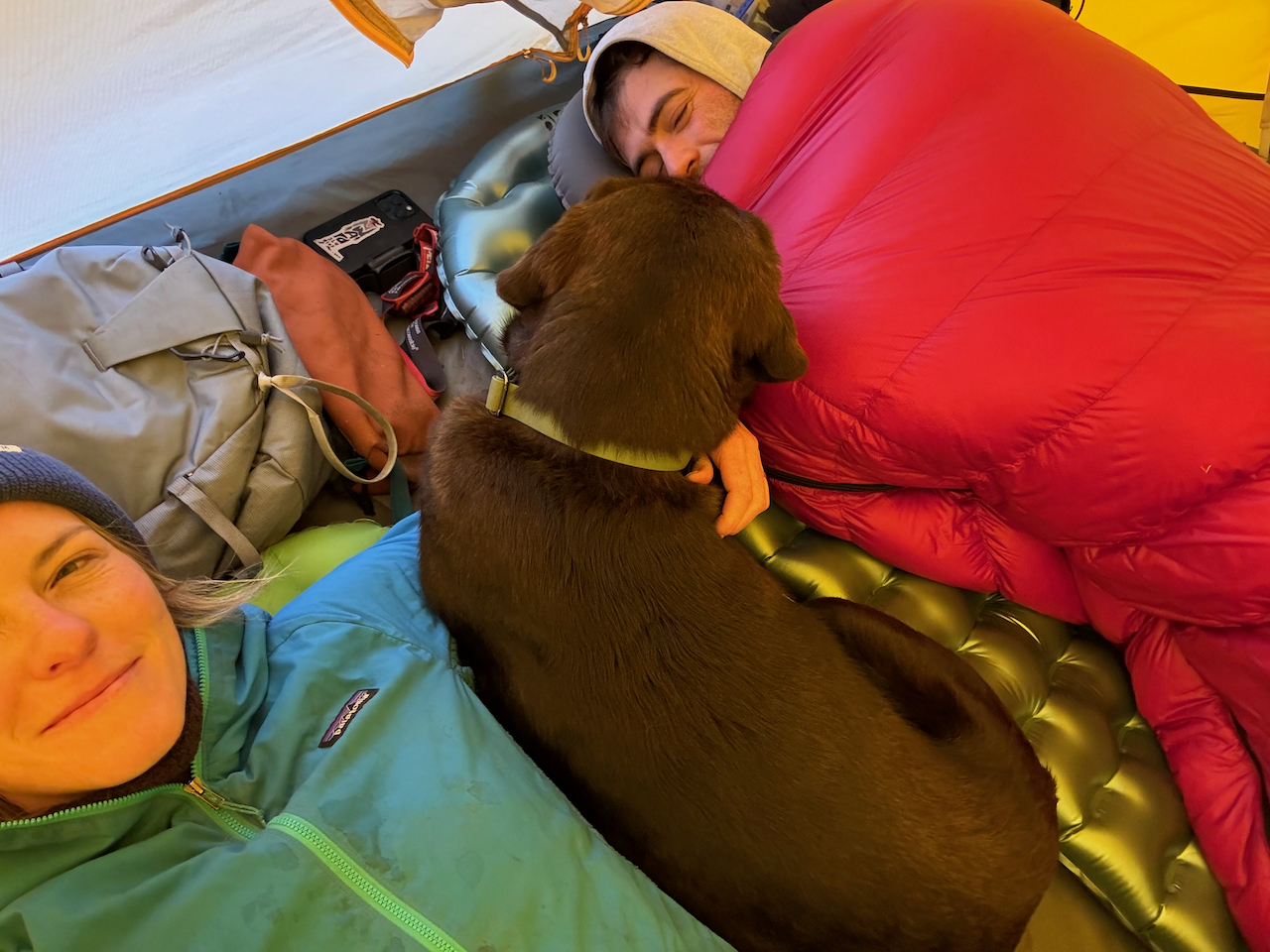man inside alpinlite sleeping bag next to woman and the dog