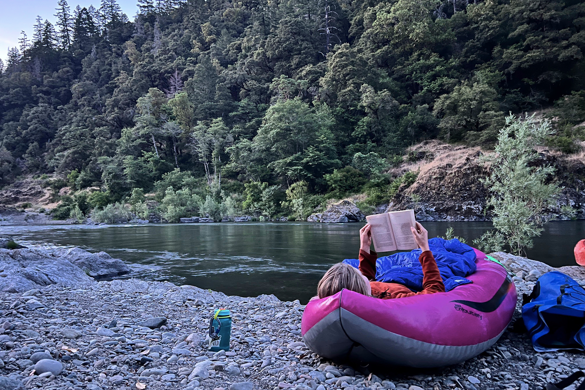 woman laying in aire spud inflatable kayak and reading a book