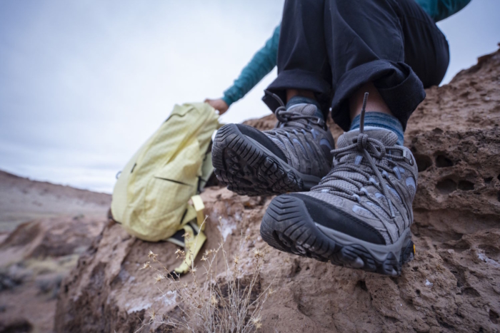 A hiker rests on a rock, with a backpack nearby, showing the soles of their hiking boots