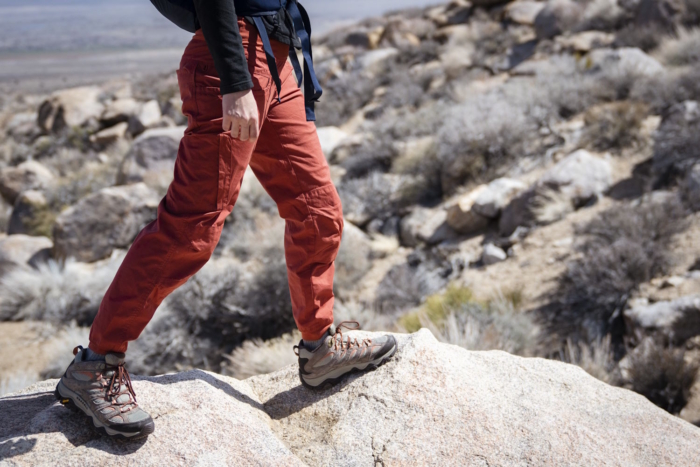 A hiker wearing red pants and Merrell Moab 3 boots walks on rocky terrain