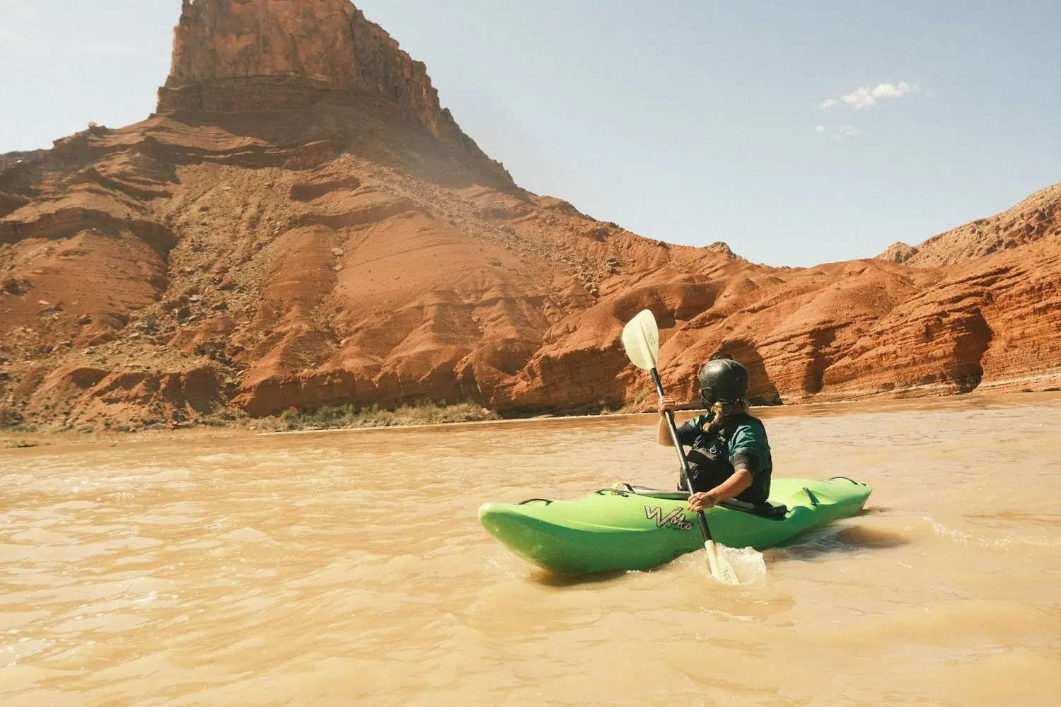 A kayaker paddling on a river with towering red rock formations in the background