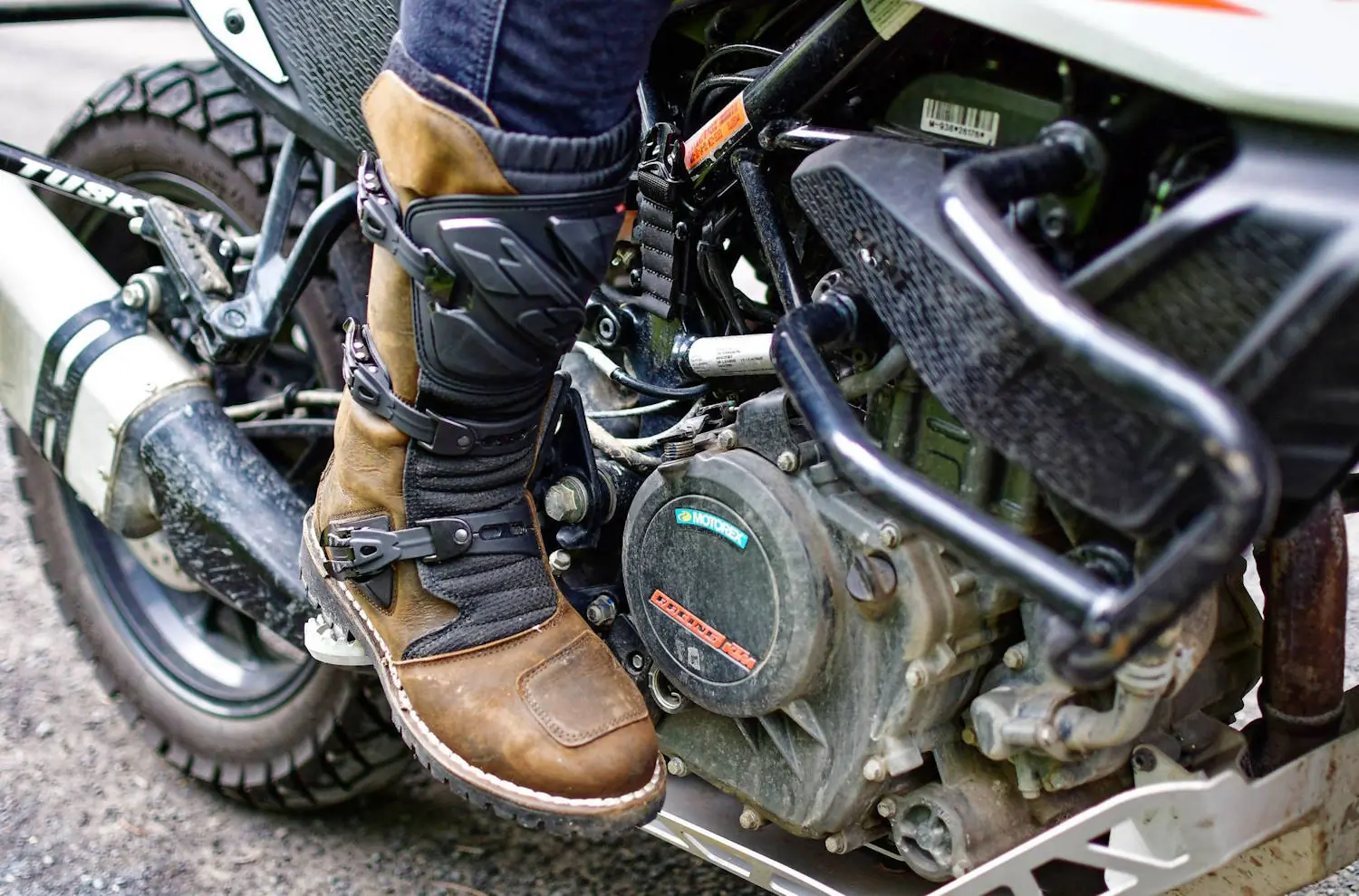 Motorcyclist's brown leather TCX Drifter adventure boot with black buckles resting on the foot peg of a dirt bike, ready for an off-road ride