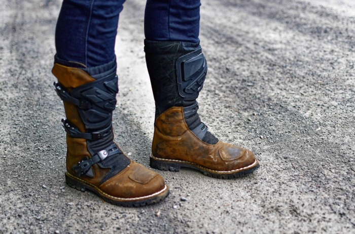 Close-up of man wearing TCX drifter WP boots with black protective gear and buckles, standing on a gravel road