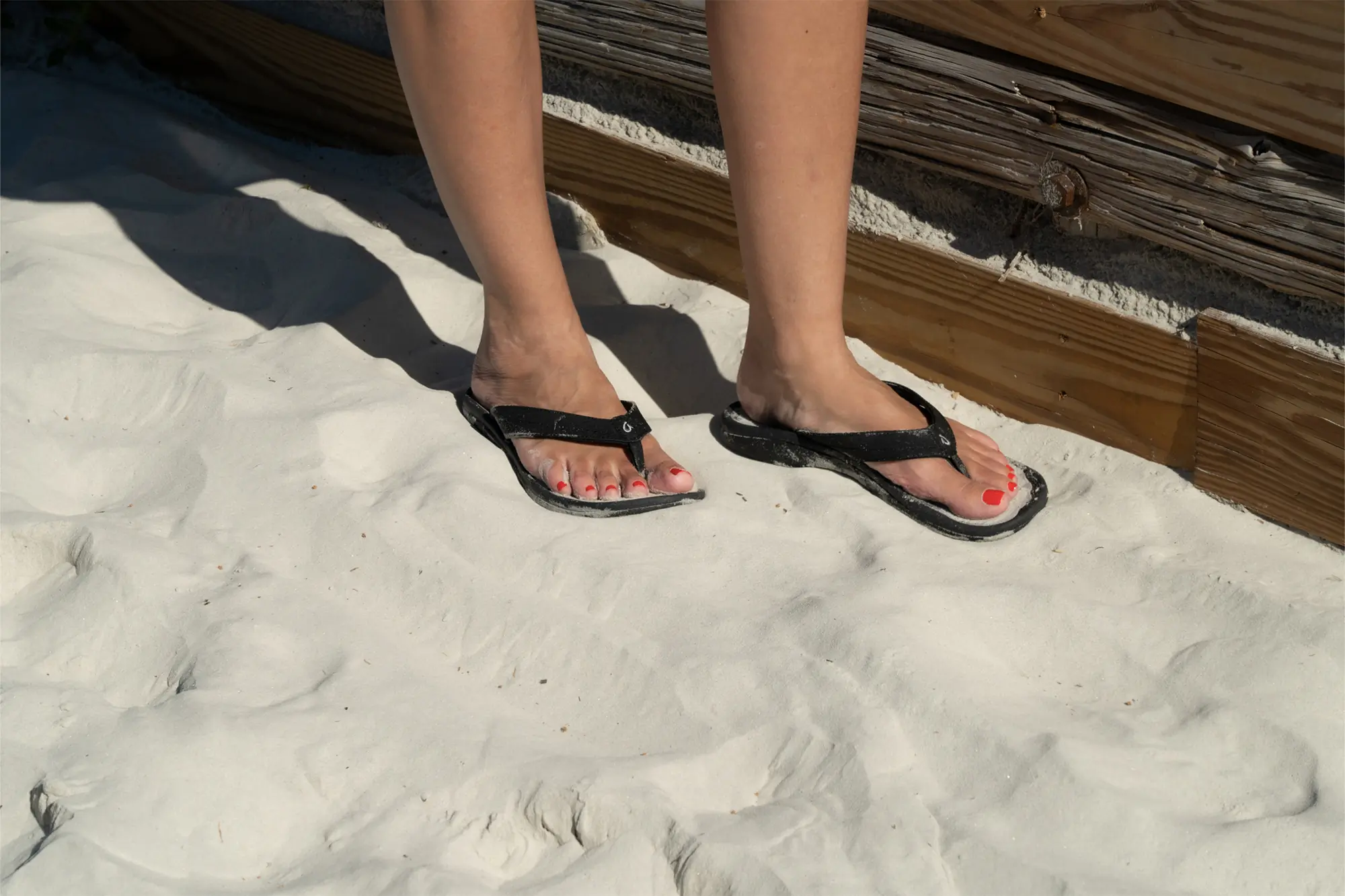 olukai flip flop close up in sand with feet