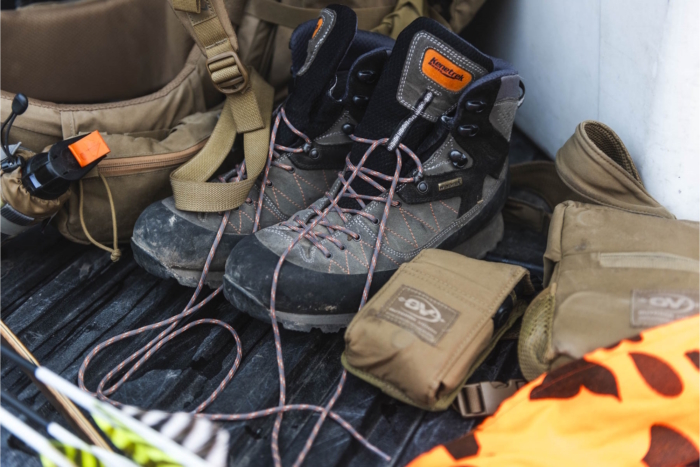 A pair of rugged Kenetrek hiking boots with laces untied, surrounded by outdoor gear