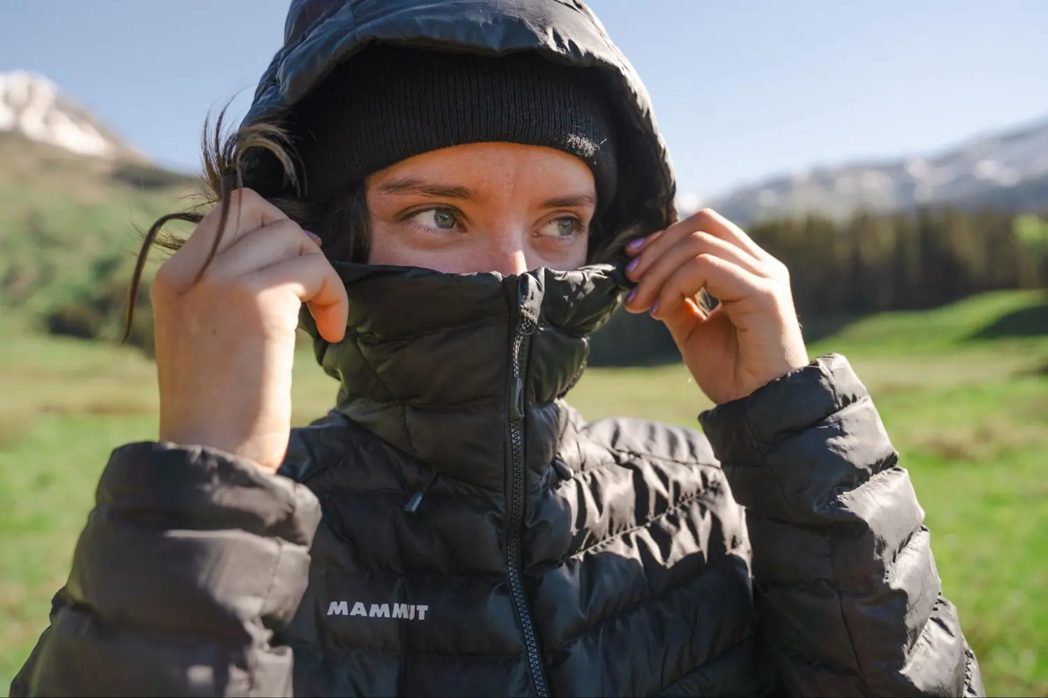 A person in a Mammut jacket and black beanie adjusting their hood