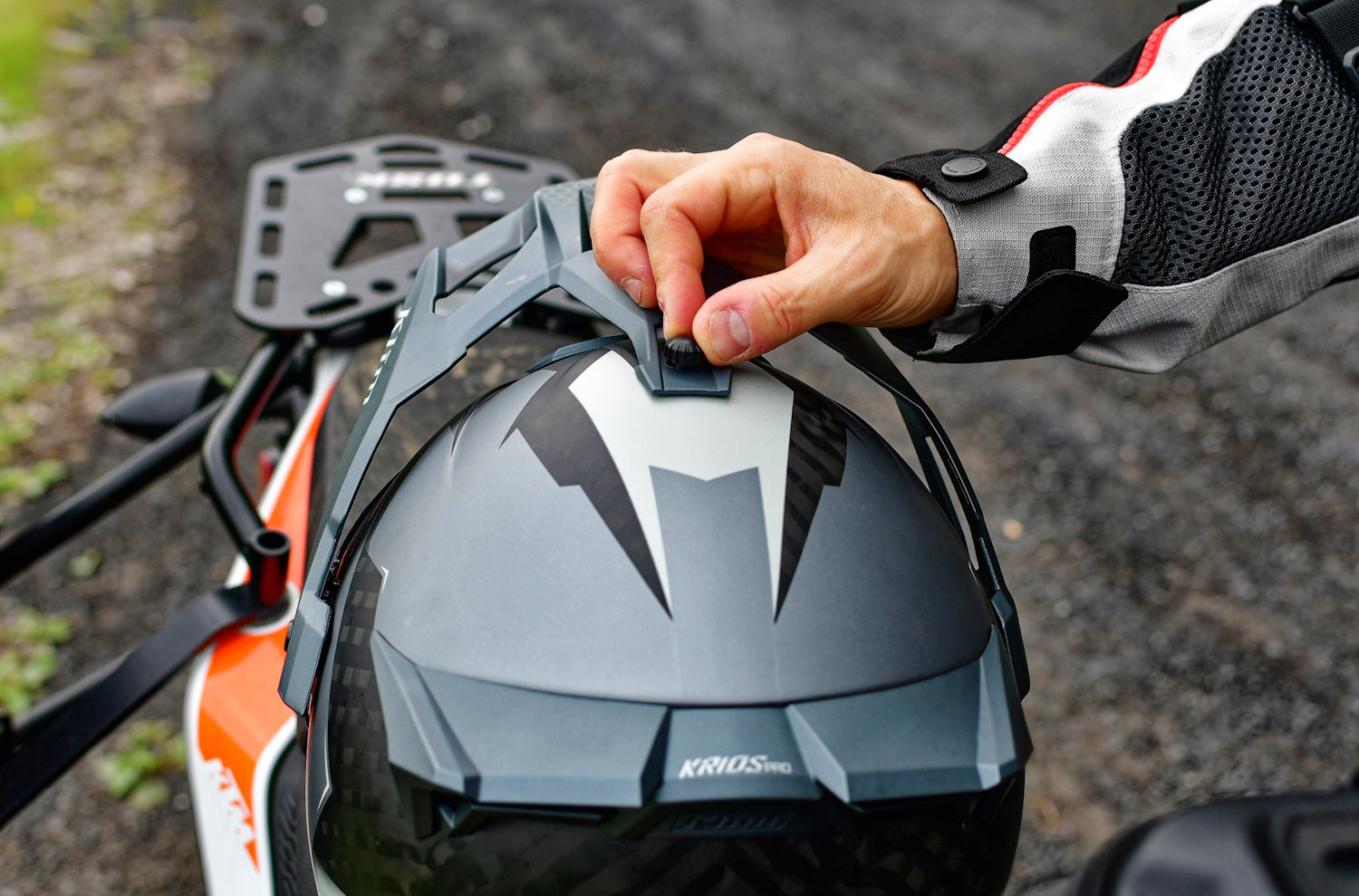 A person adjusts the peak of a grey Klim Krios Pro motorcycle helmet