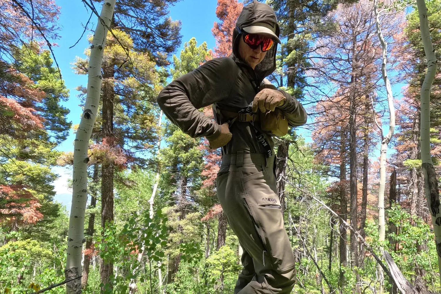 A person in outdoor gear, adjusting their backpack straps while standing in a sunlit forest