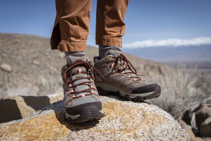 A person standing on a rock wearing gray and orange moab 3 hiking shoes with brown pants
