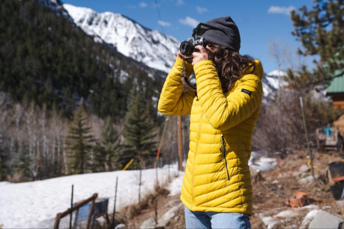 A person in a yellow Decathlon Forclaz MT100 Hooded Down Puffer Jacket taking photos with a camera in a snowy mountain landscape