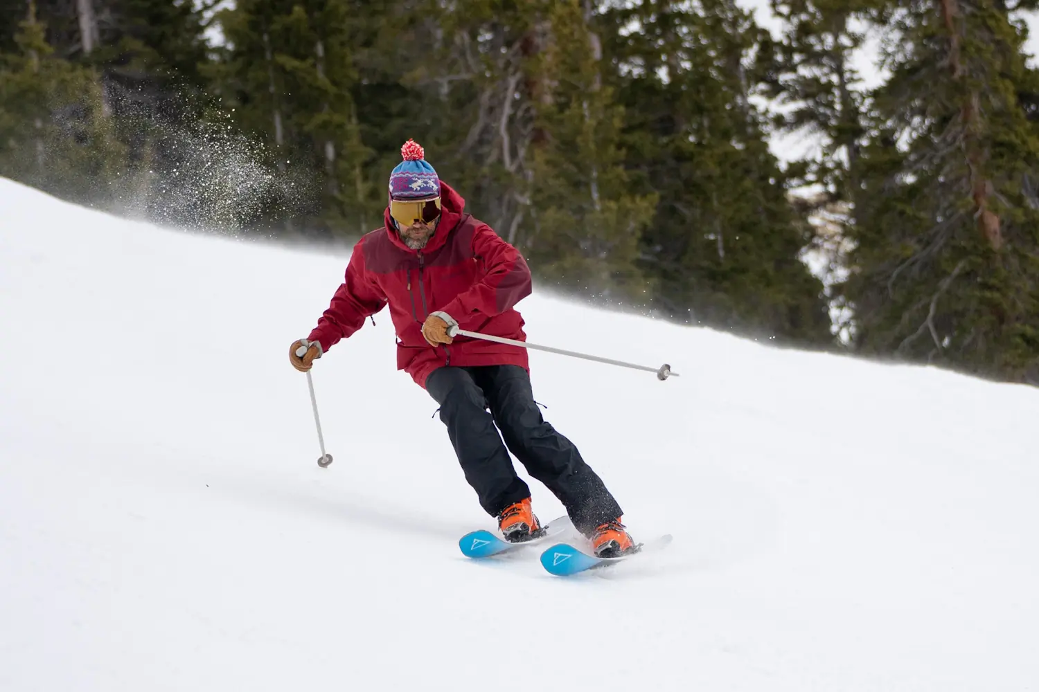 A skier in a red jacket and blue hat rides down a slope on Renoun Endurance 98 skis