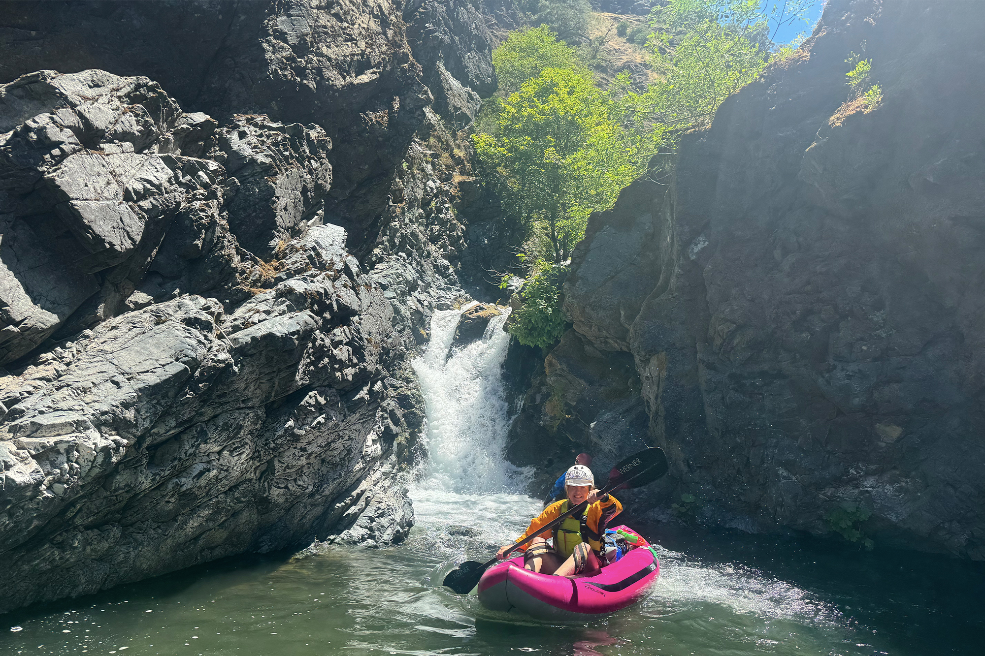 woman in aire tributary spud inflatable kayak next to rocks and waterfall