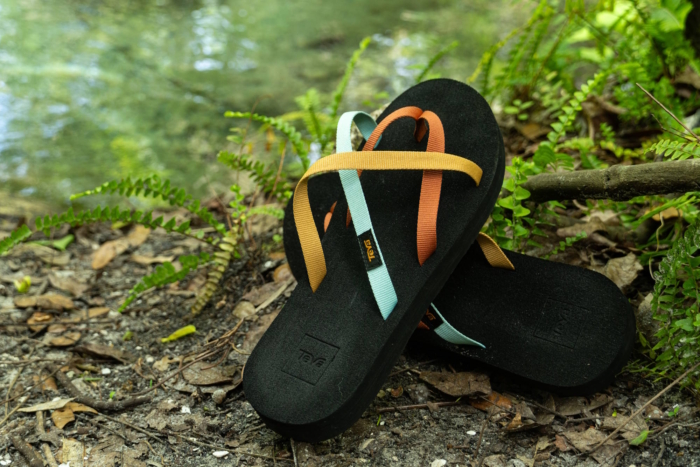 A pair of black flip-flops with multicolored straps resting on the ground surrounded by greenery