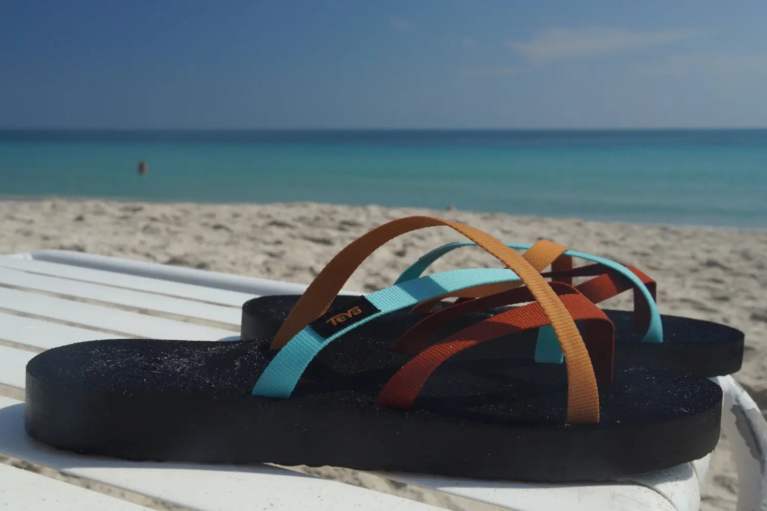 A pair of Teva Olowahu flip-flops resting on a beach chair with the ocean in the background