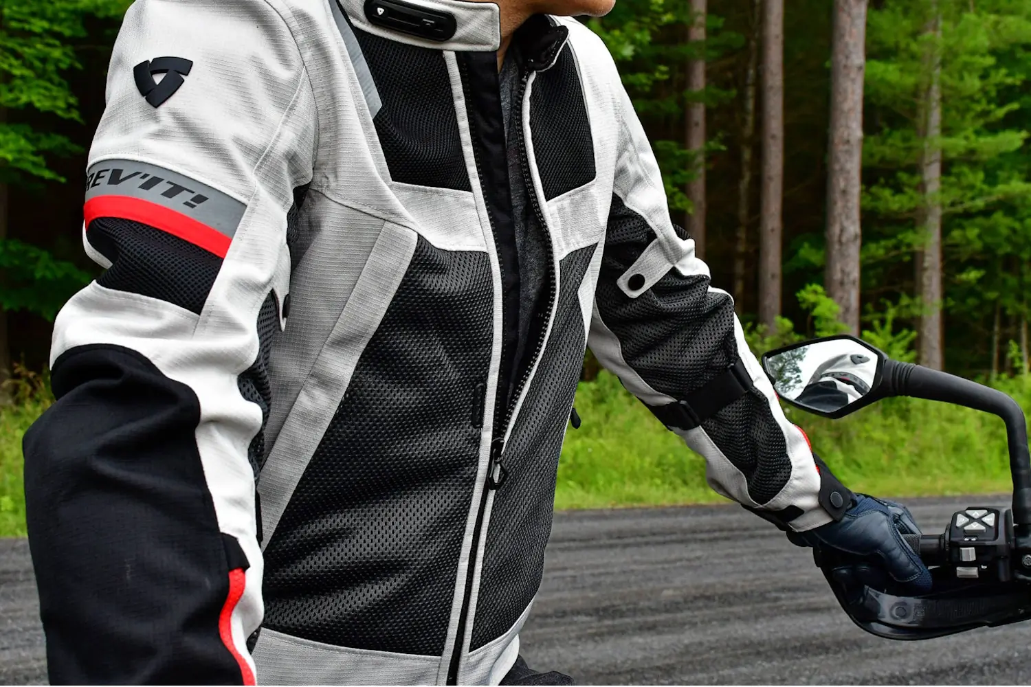 A person wearing a Rev'it! motorcycle jacket, featuring multiple zippers